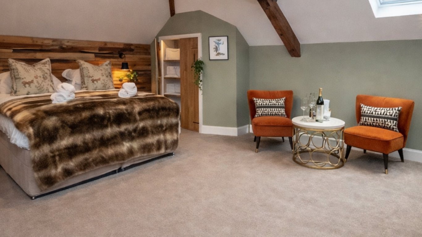 Luxurious attic bedroom with striped upholstered bed, exposed wooden beams, orange accent chairs, and green walls with skylight