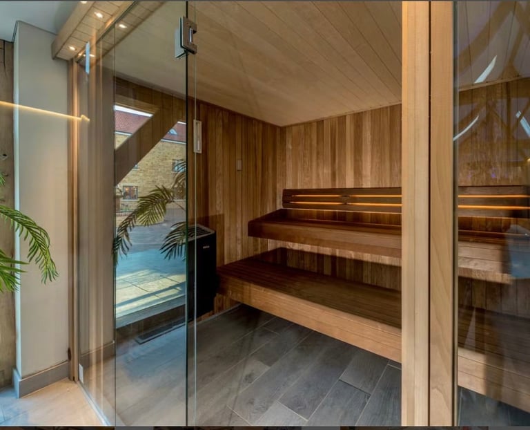 Modern sauna interior with wooden benches, glass door, and pool view through windows